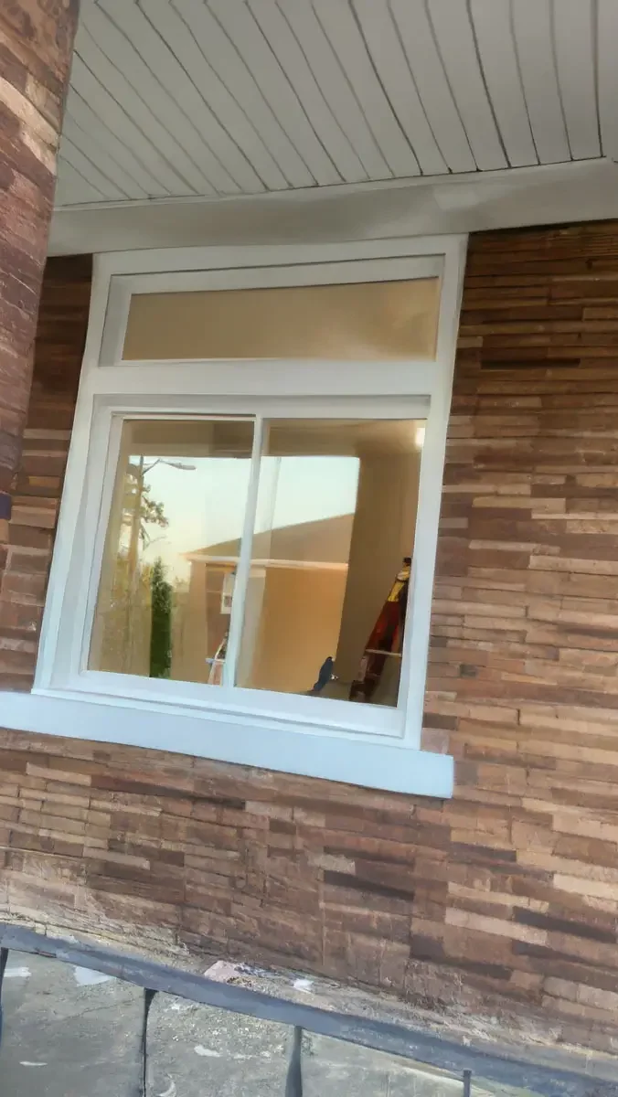 A window installed sideways on a wooden exterior wall, with a house reflected in the glass.